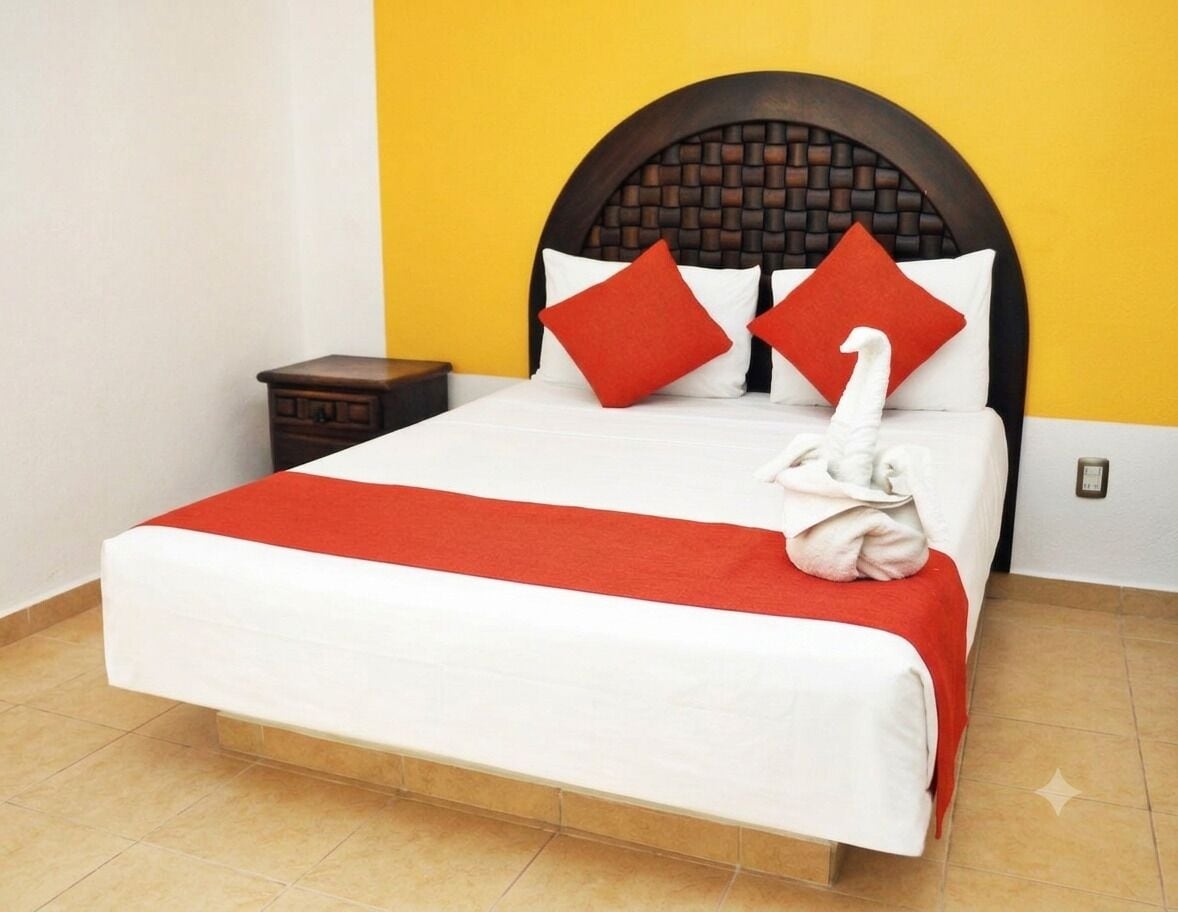 A bed with a white mattress, red and white bedding, and a towel on the side.