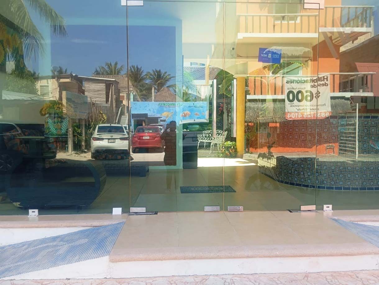 Entrada de hotel con puerta de cristal, zona de estacionamiento con automóviles y un letrero que indica capacidad para 1000 habitaciones.