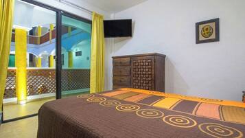 A hotel room with a bed, a TV, a wooden cabinet, and a balcony with yellow curtains.