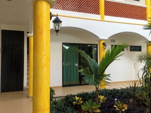 A building with yellow pillars, a green door, and a small palm tree in the foreground.