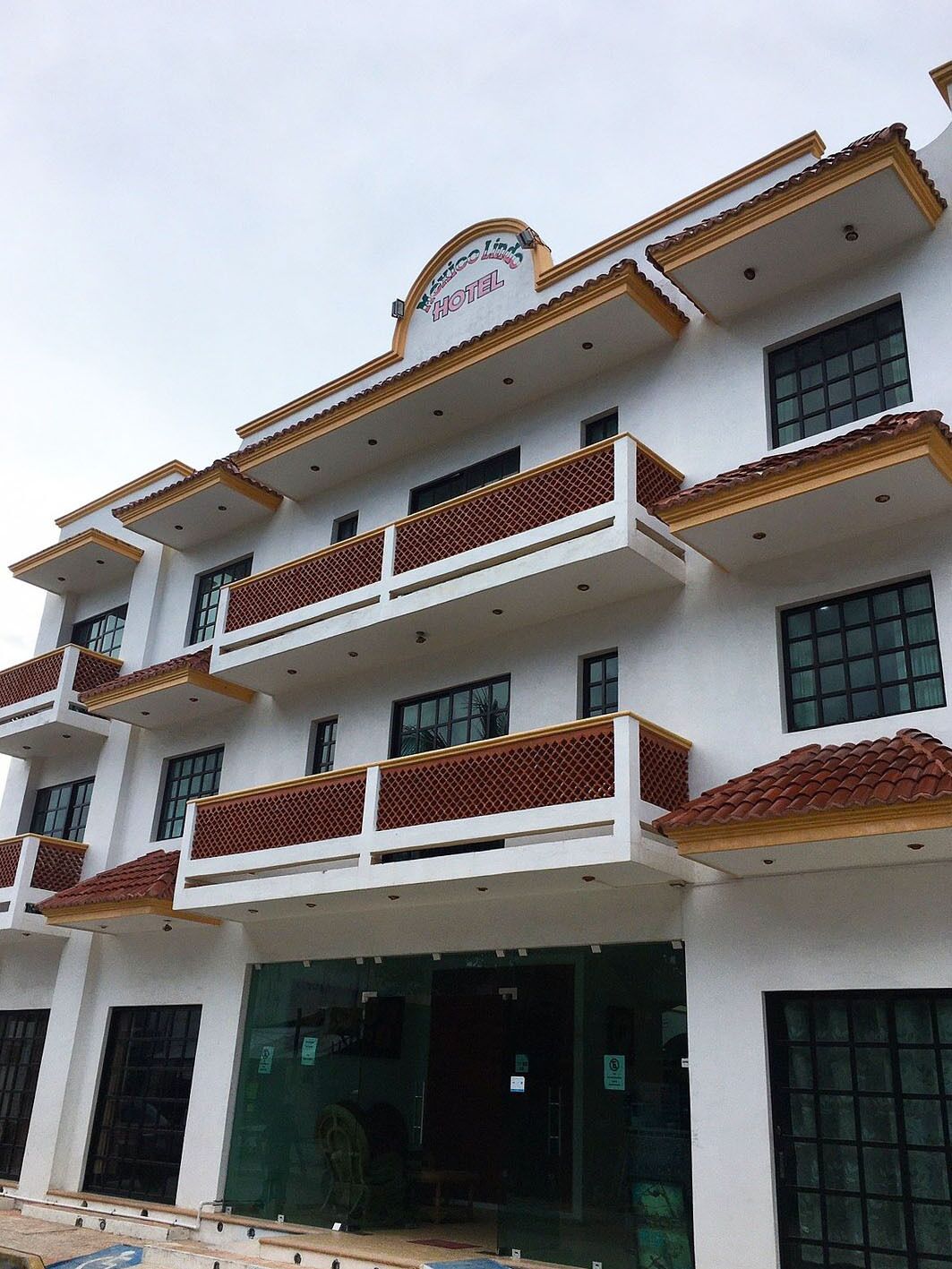Un hotel de varios pisos con balcones, una señal que indica que es un hotel y una entrada amplia con puertas de cristal.