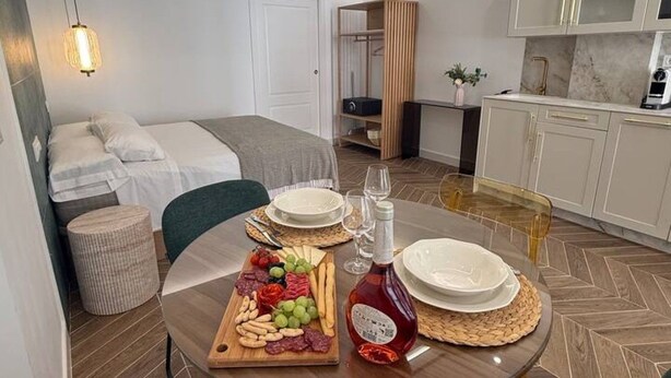 Ein modernes Hotelzimmer mit Bett, Esstisch mit Obstplatte und einer Küchenzeile.