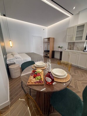 Ein modernes Hotelzimmer mit Bett, Esstisch mit Obstplatte und einer Küchenzeile.