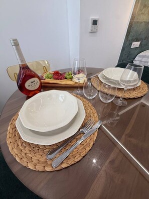 Une table à manger dressée avec de l’assiette blanche, des couverts en argent et une bouteille de vin Mateus.