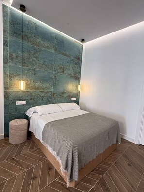 Ein modernes Schlafzimmer mit einem Bett, einem Kopfteil mit Wandleuchten und einem Fischgrätenparkettboden.