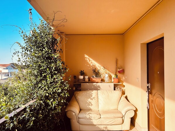 A balcony with a beige sofa, potted plants, and a wooden door.