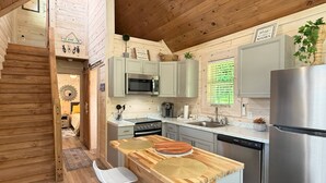 Una cocina compacta con armarios de madera, un refrigerador de acero inoxidable y un pequeño comedor con dos sillas blancas.