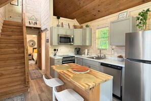 Eine kompakte Küche mit Holzschränken, einem Edelstahlkühlschrank und einer kleinen Essecke mit zwei weißen Stühlen.