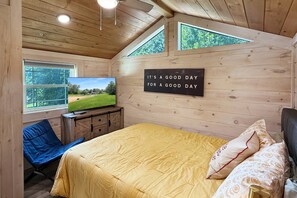 Une chambre dans une cabane en bois, comprenant un lit, une télévision, un bureau et une fenêtre donnant sur un paysage verdoyant.
