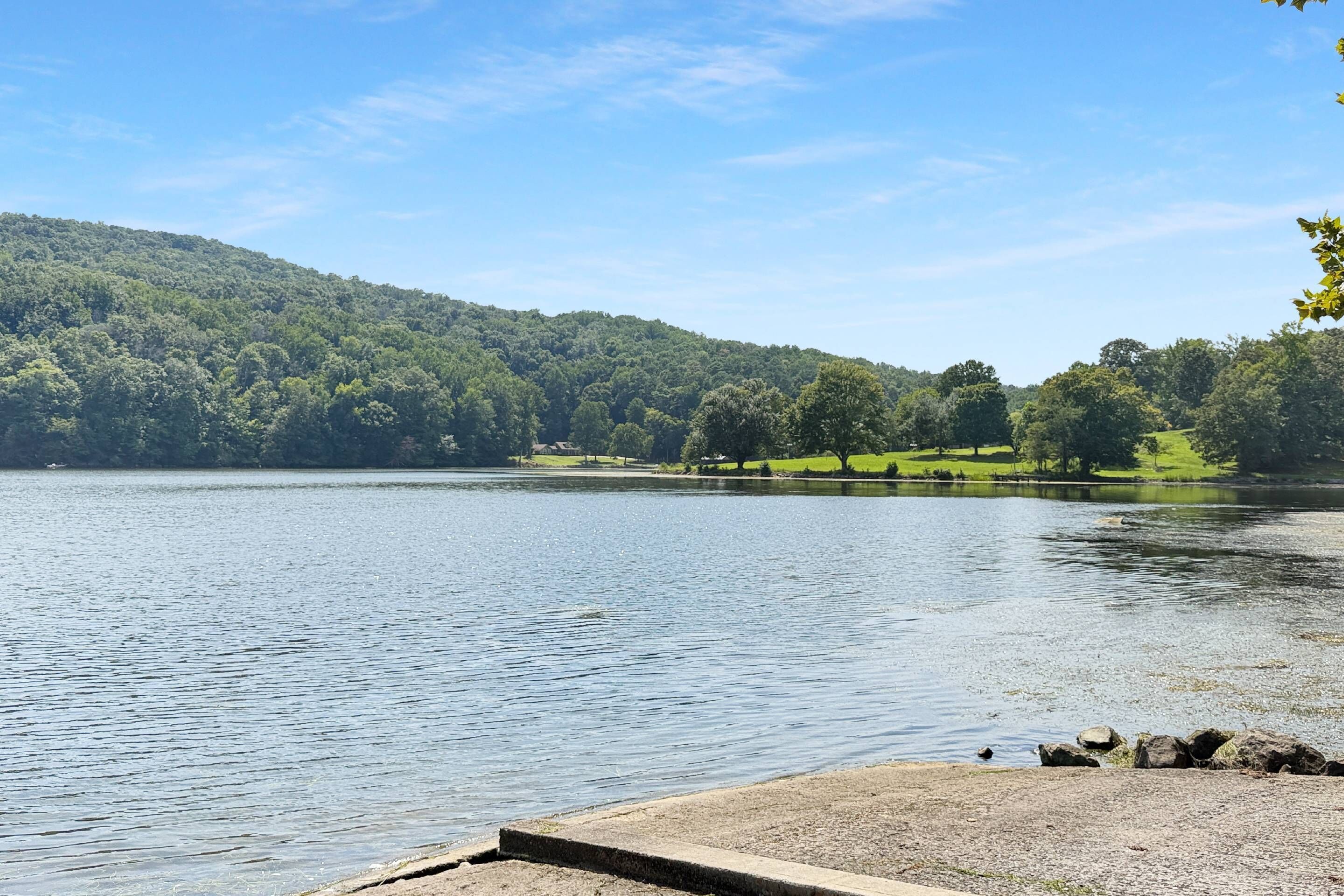 Un lac paisible avec un quai, entouré de collines verdoyantes et sous un ciel dégagé.