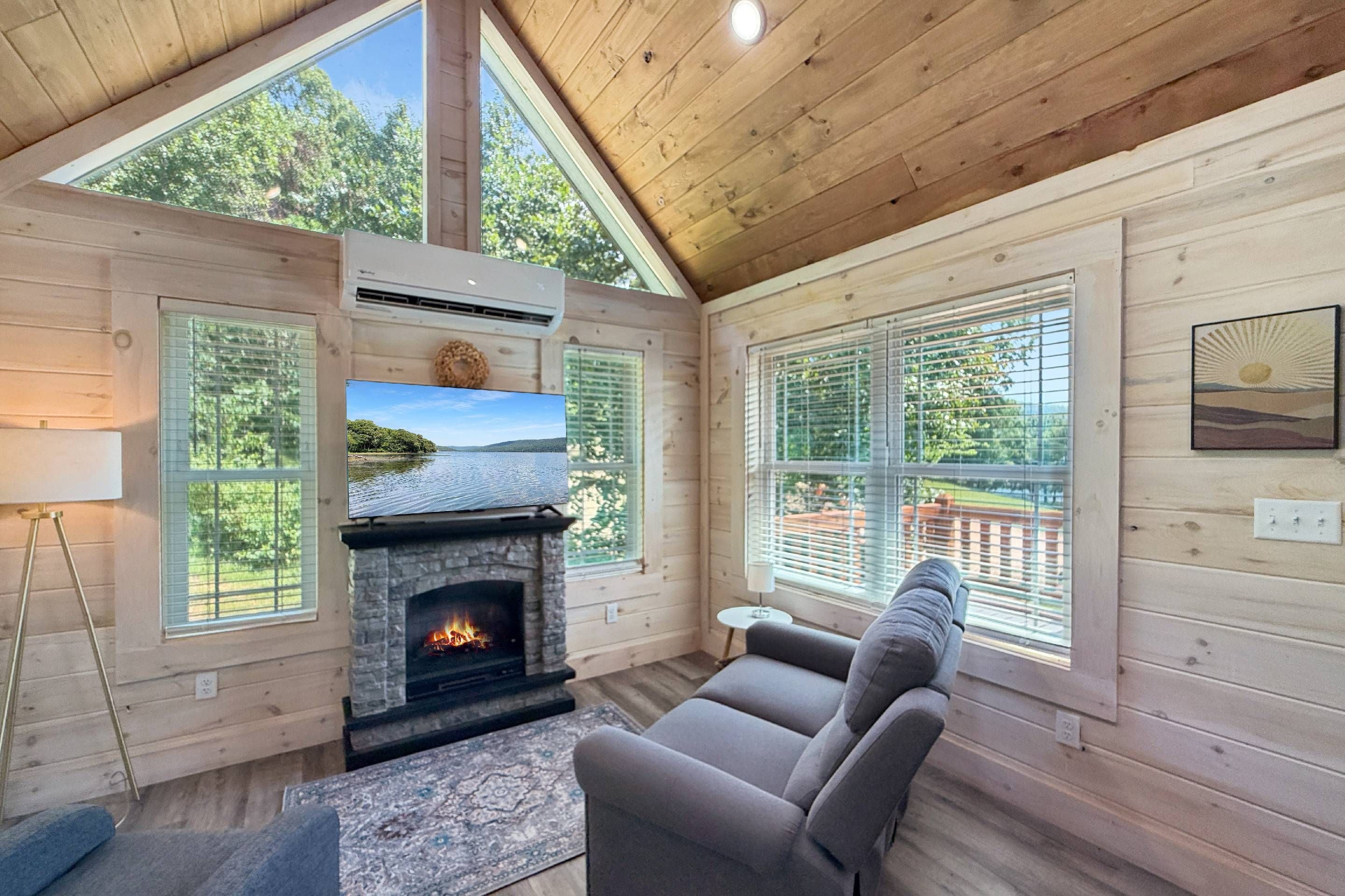 L’intérieur chaleureux d’un chalet avec une cheminée en pierre, un canapé confortable et de grandes fenêtres donnant sur le paysage extérieur.
