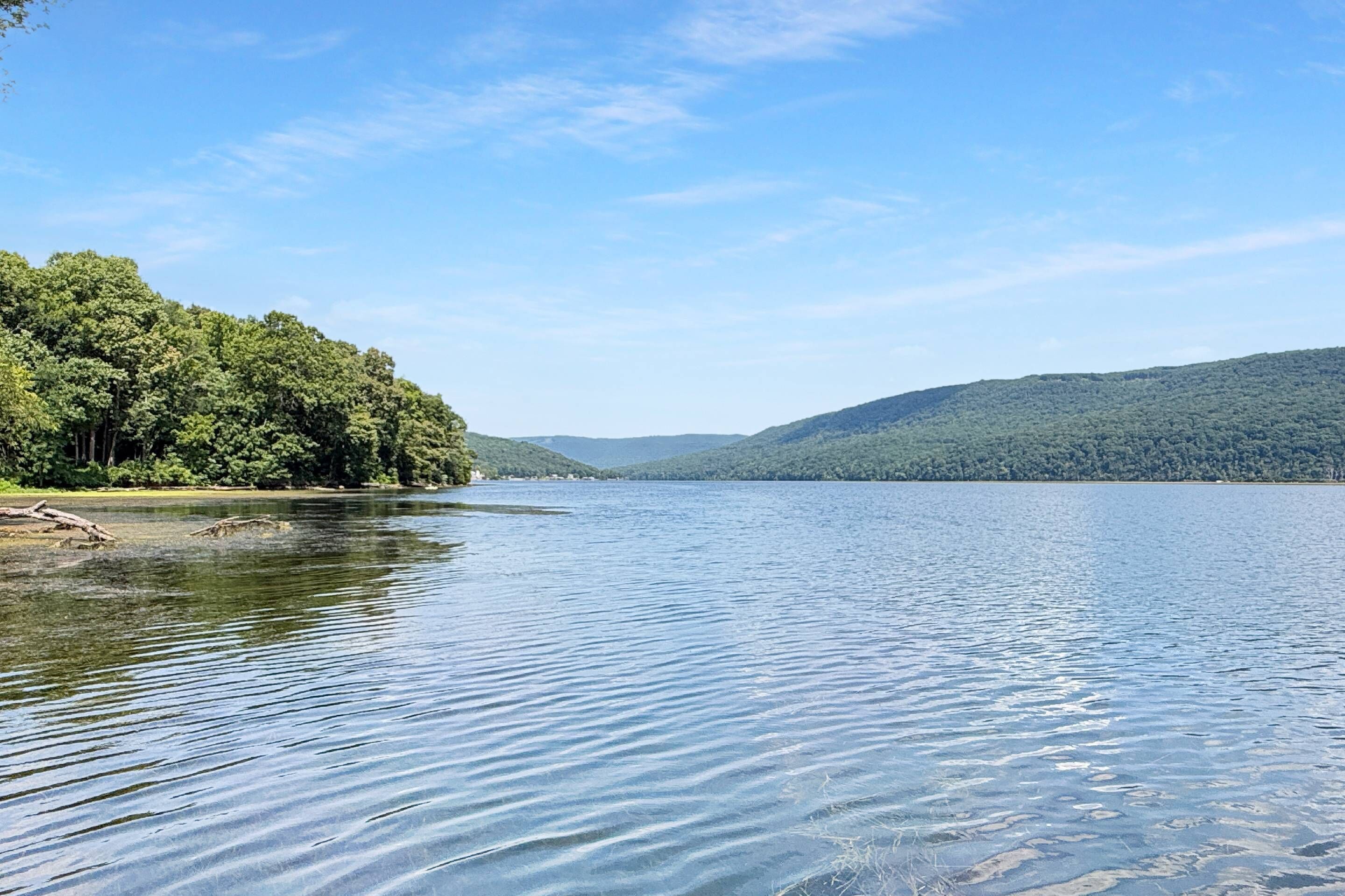 Um lago calmo com margens arborizadas e colinas ao longe.