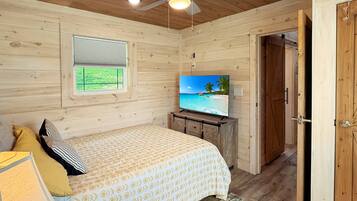 A bedroom with a bed, a television, a ceiling fan, and a window.