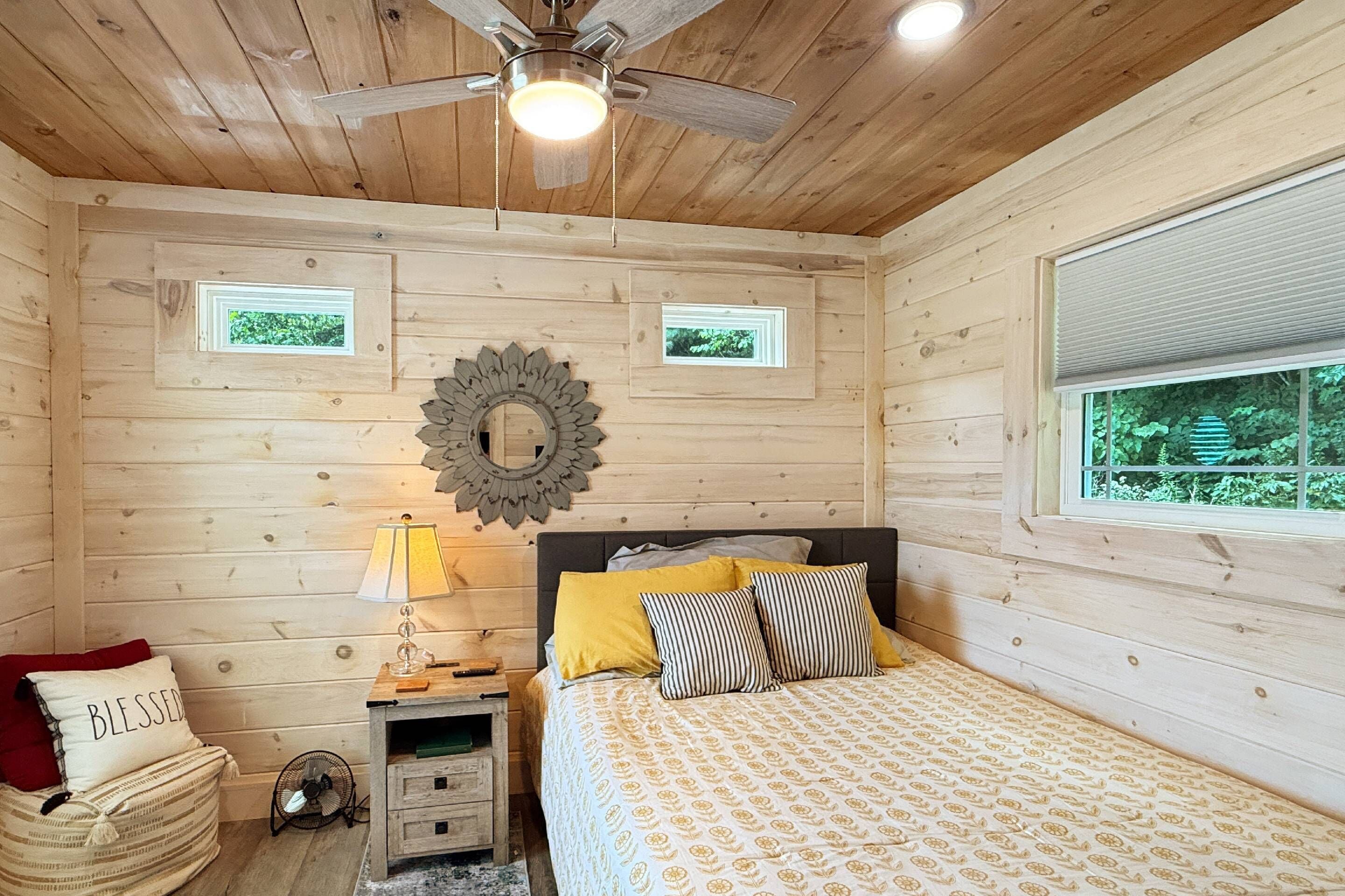 A wooden room with a bed, a nightstand, a lamp, and a ceiling fan.