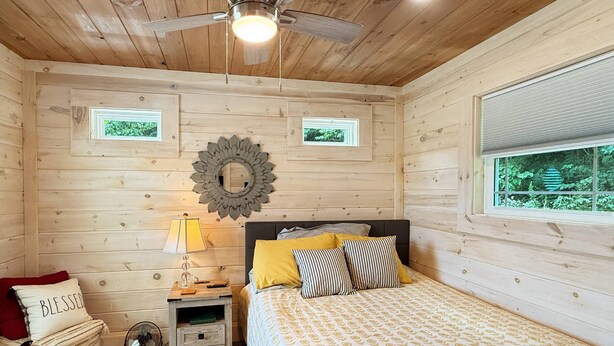 Una habitación de madera con cama, mesita de noche, lámpara y ventilador de techo.