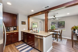 A modern kitchen with a central island, stainless steel appliances, and a dining area with a view. - The River's Edge - Private Home with River Access, Spa, and Karaoke (Three Rivers)