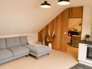 A modern living room with a grey sectional sofa, a white vase with dried plants, and a wooden wall.