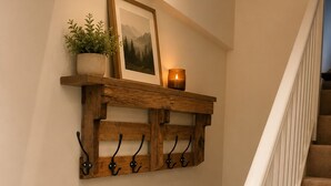 Una scala con uno scaffale a muro in legno sopra, dove sono posti una pianta, una candela e un quadro incorniciato.
