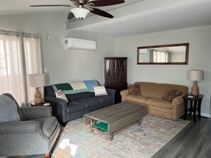 Un salon avec un ventilateur de plafond, deux canapés, une table basse, un meuble et un miroir.