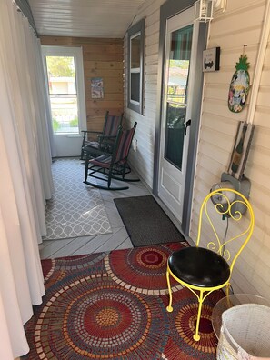 A covered porch with rocking chairs, a yellow chair, and a wicker basket. - Cozy 2-bedroom cottage - St Clair River access in beautiful Algonac with AC (Algonac)