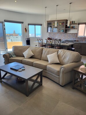 Ein modernes Wohnzimmer mit einer Couch, einem Couchtisch und Blick auf die Stadt durch große Fenster.