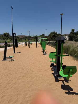 Trainingsgeräte im Freien auf sandigem Untergrund bei blauem Himmel.
