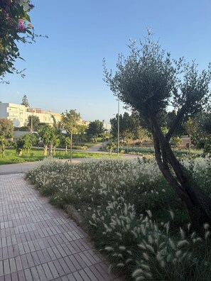 A paved walkway with grass and trees, a clear sky, and buildings in the background. - Charming 3-bedroom house in Agadir Near the Beach perfect for your getaway (AGADIR)