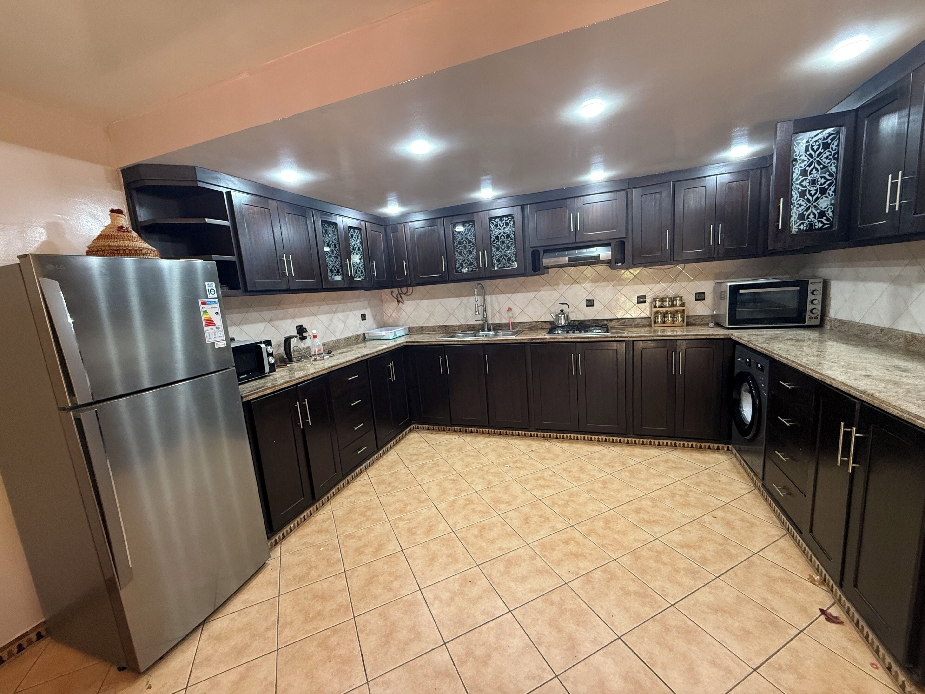 A kitchen with dark cabinets, a stainless steel refrigerator, a microwave, and a tiled floor.