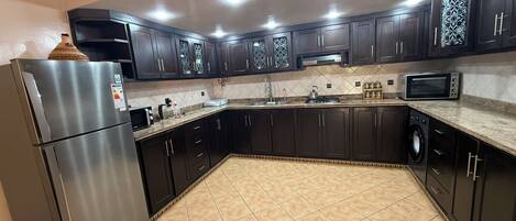A kitchen with dark cabinets, a stainless steel refrigerator, a microwave, and a tiled floor.