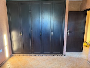 A large, dark-colored wardrobe with multiple doors and handles, situated in a room with tiled flooring and a partial view of a door on the right.