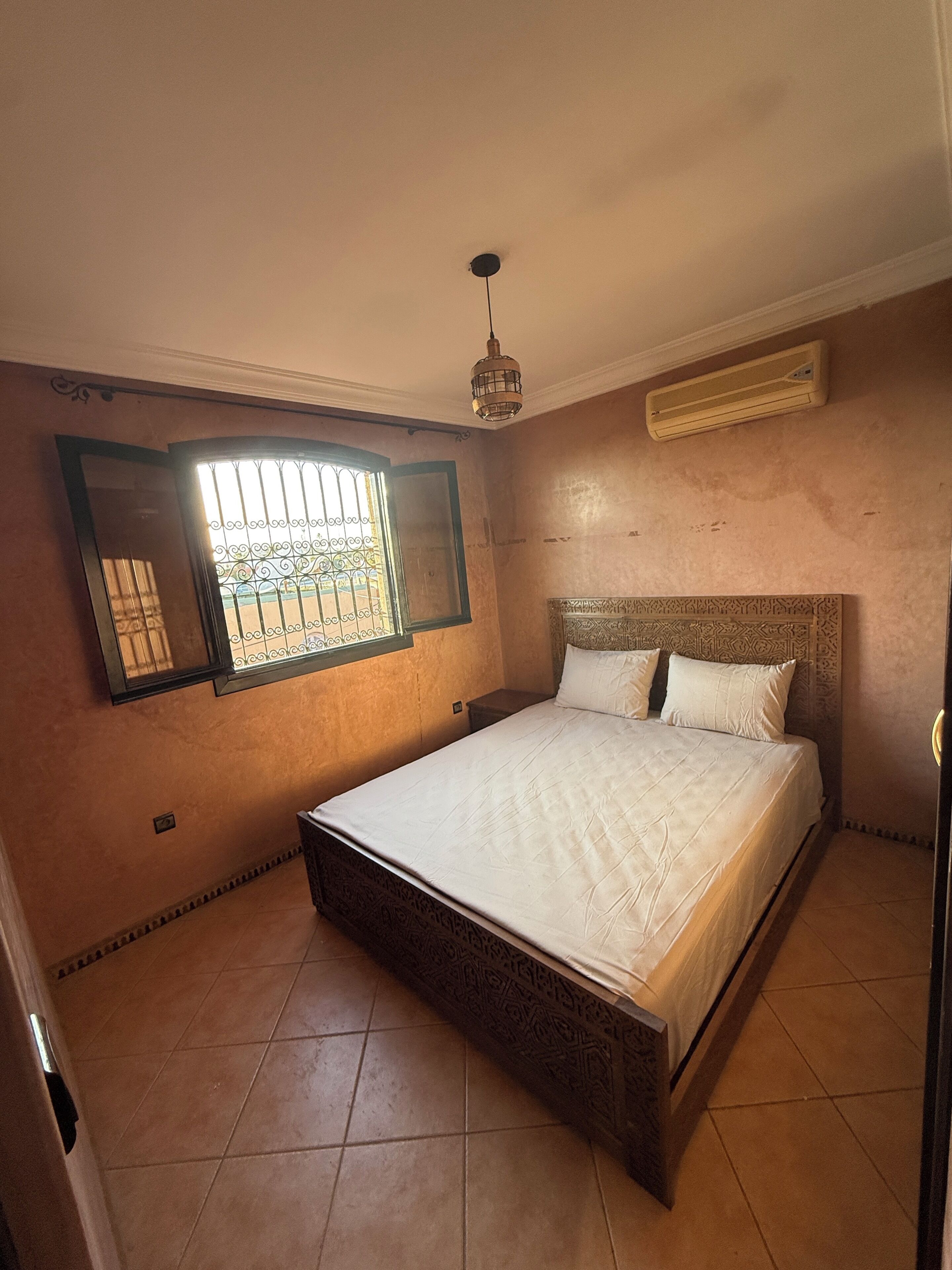 Una camera da letto con un letto, una finestra con le sbarre, un ventilatore a soffitto e un condizionatore d'aria.