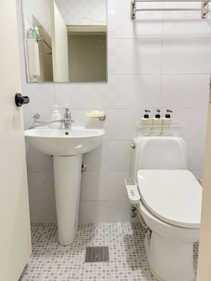 Casa de banho com lavatório branco, sanita e espelho.