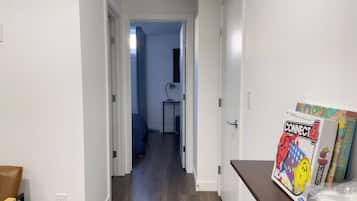 A hallway with a wooden floor, a desk with a lamp, and a door leading to a room.