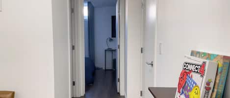 A hallway with a wooden floor, a desk with a lamp, and a door leading to a room.