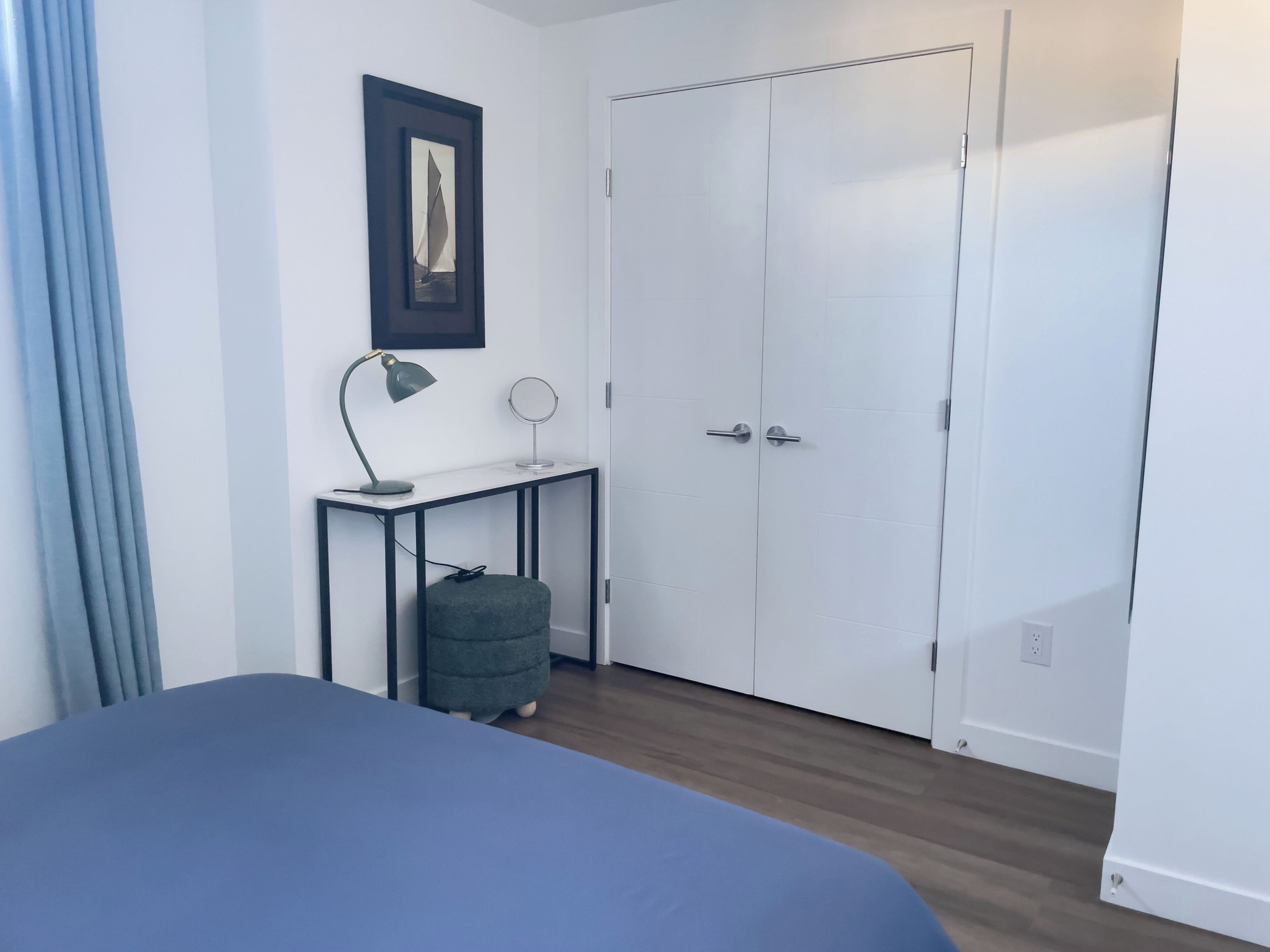 A bedroom with a bed, a desk with a lamp, a chair, and a wardrobe.