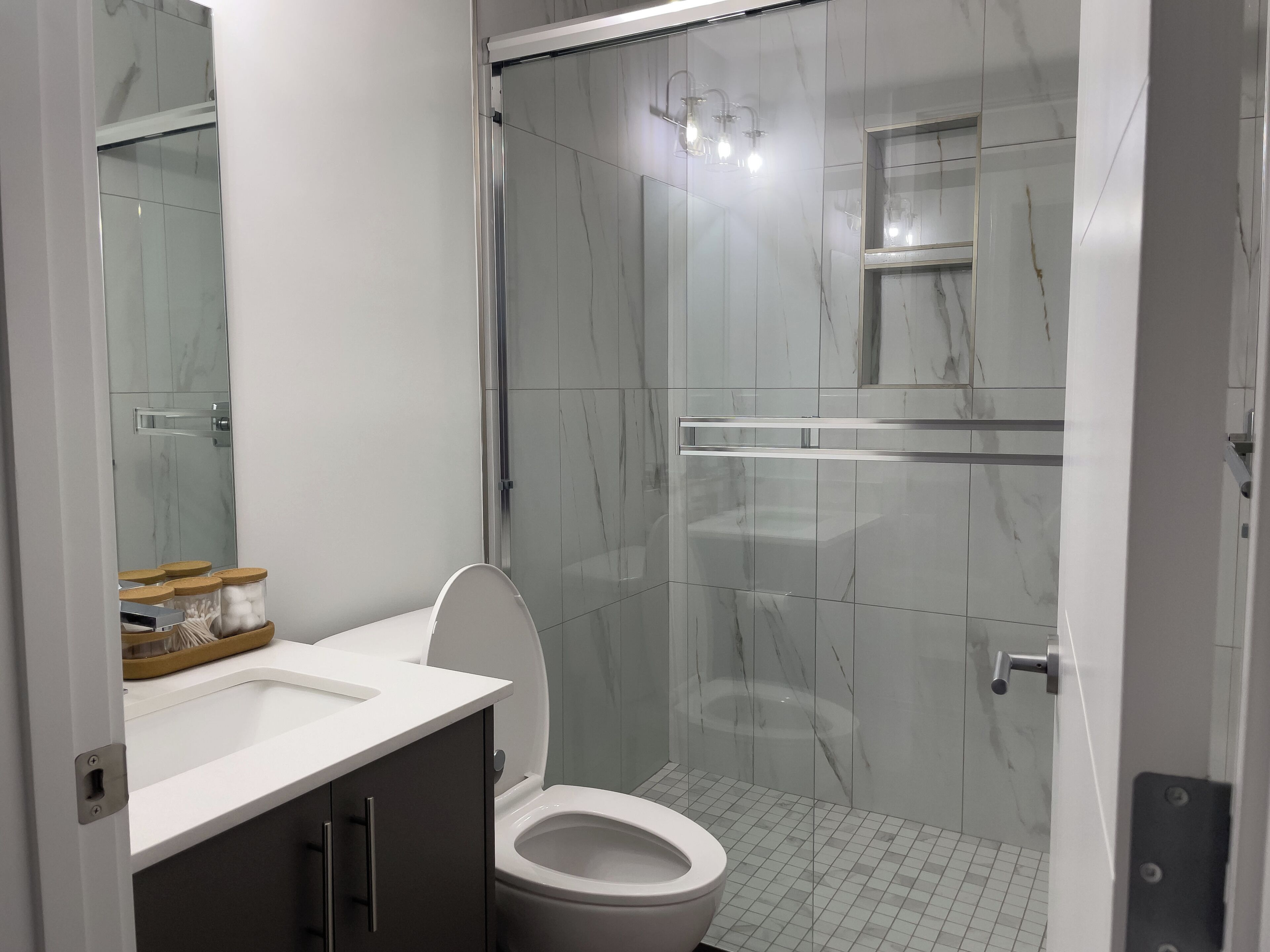 Une salle de bain moderne équipée de toilettes, d’une douche et d’un meuble-lavabo avec un miroir.