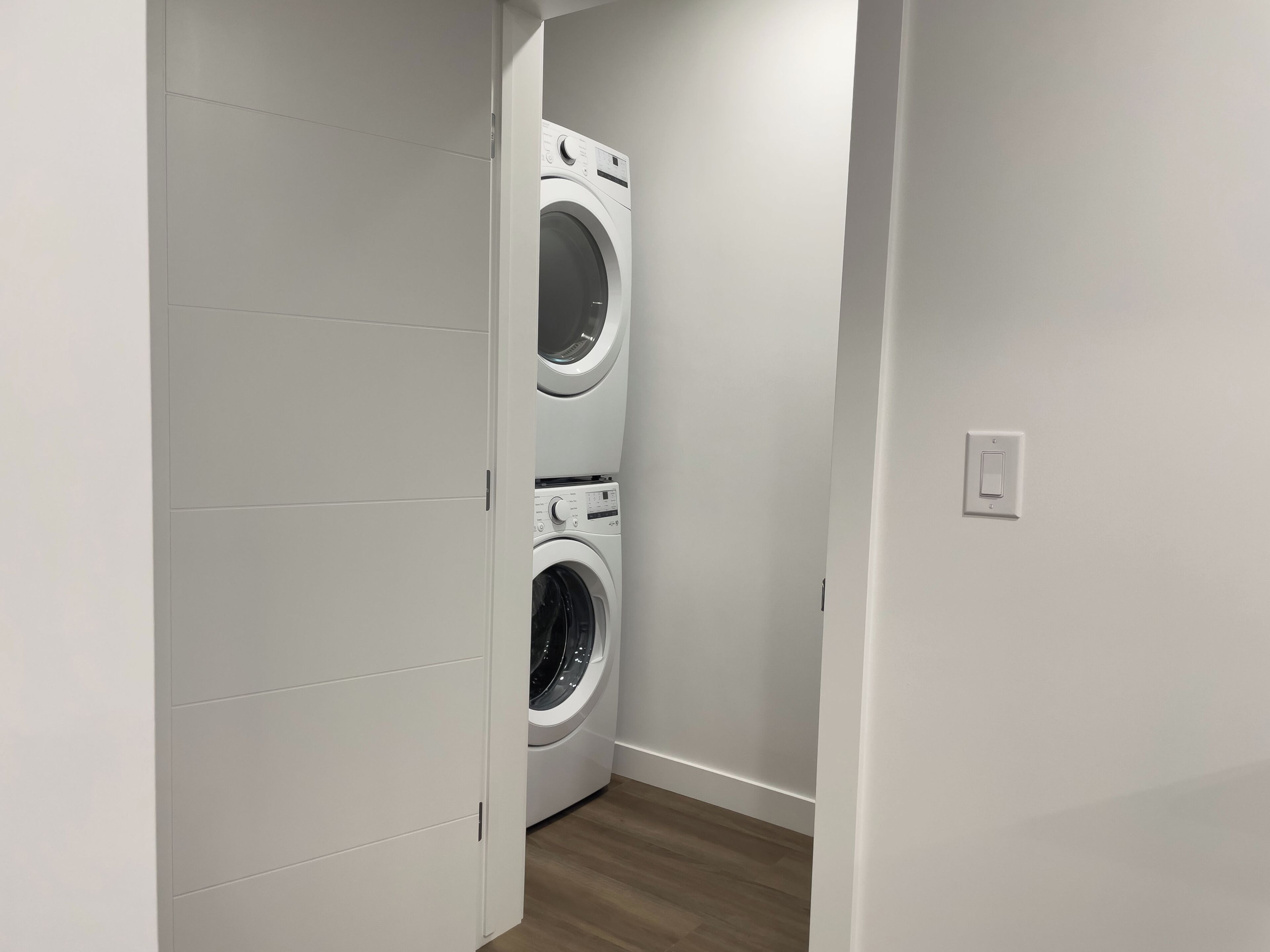 A laundry room with two stacked washing machines and a wooden floor.