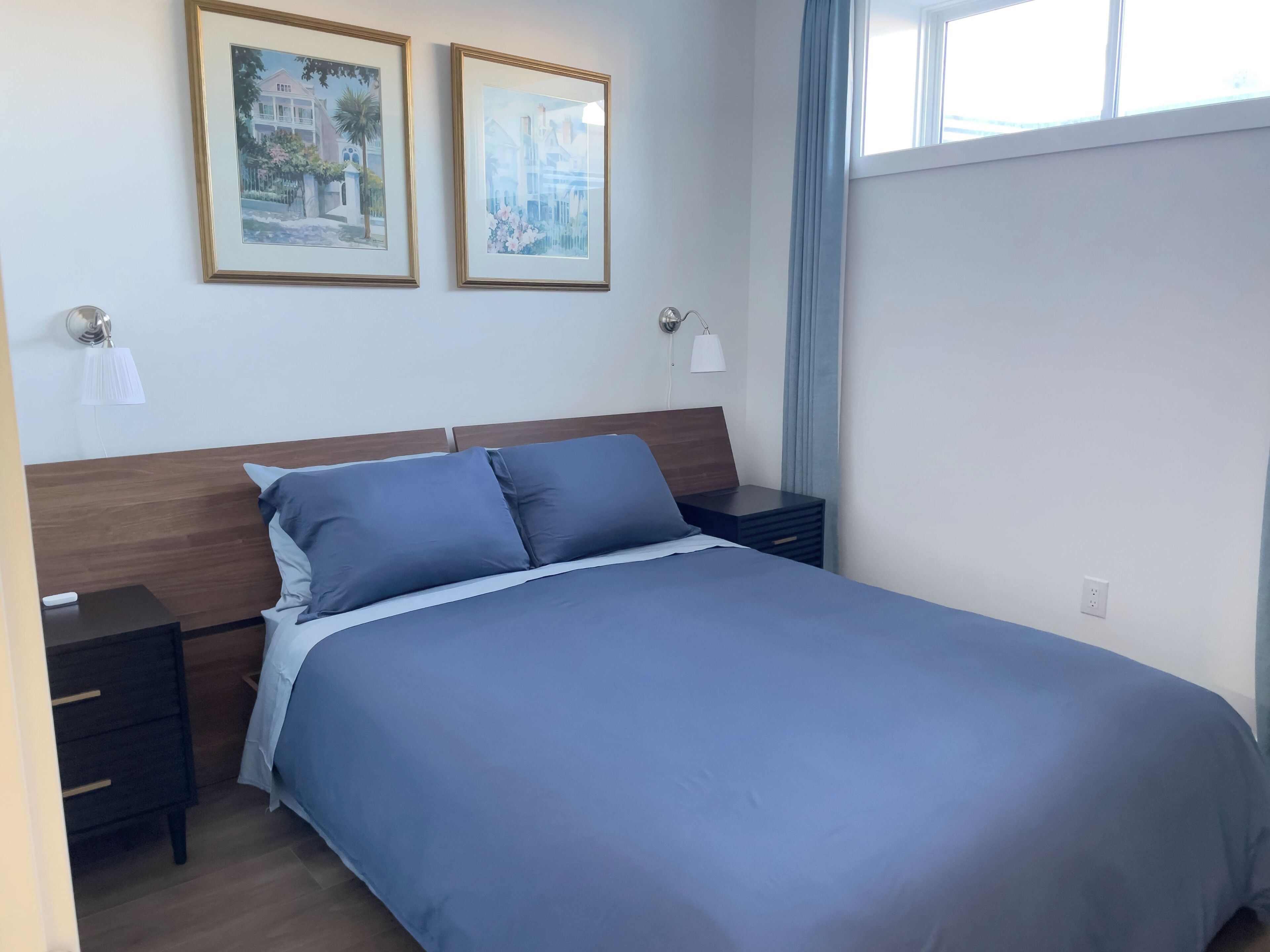 Un lit bien fait, avec une couvre-lit bleue et des oreillers, deux tables de chevet avec des lampes et deux tableaux encadrés accrochés au mur.