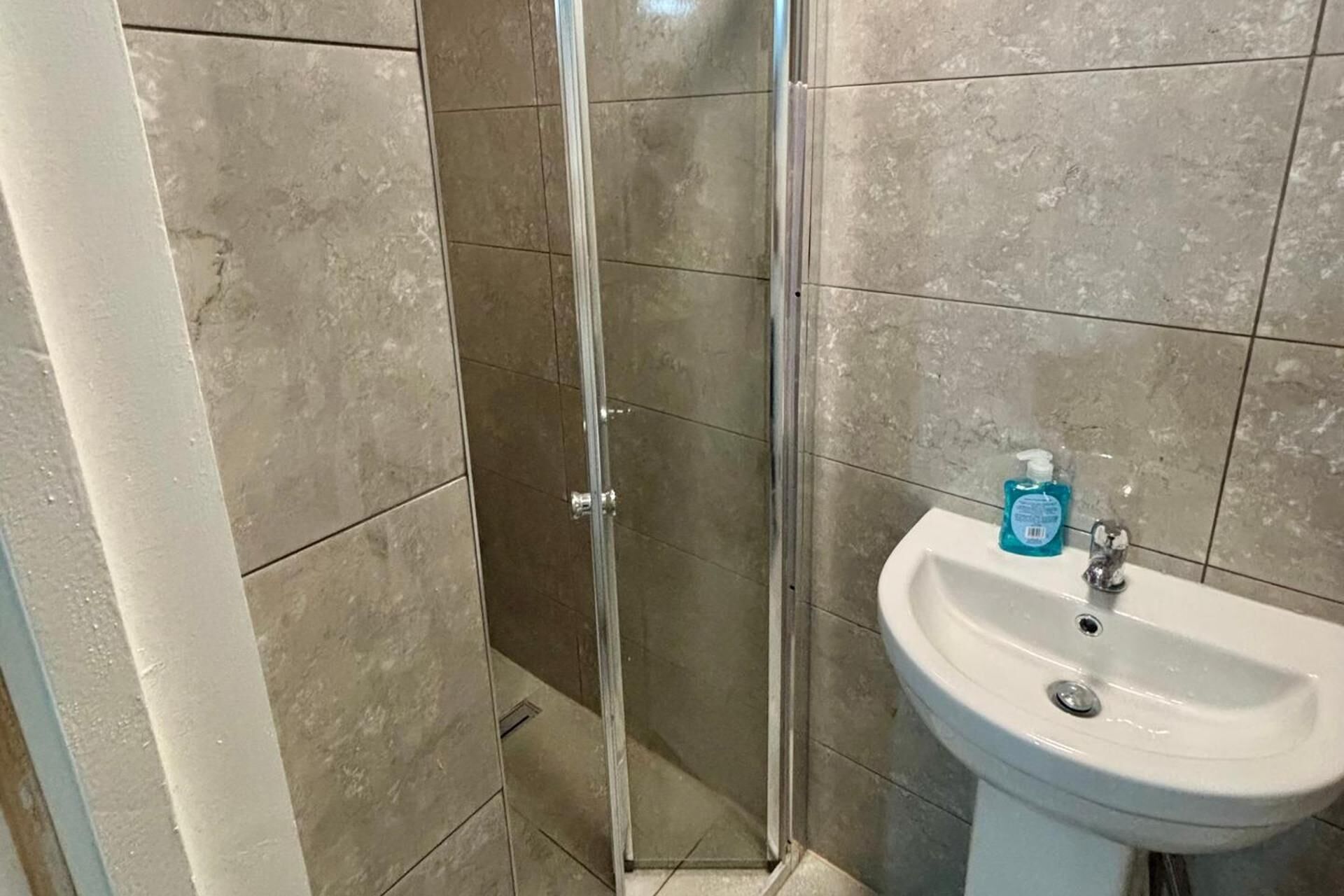 A bathroom with a glass shower enclosure and a white sink with a soap dispenser.
