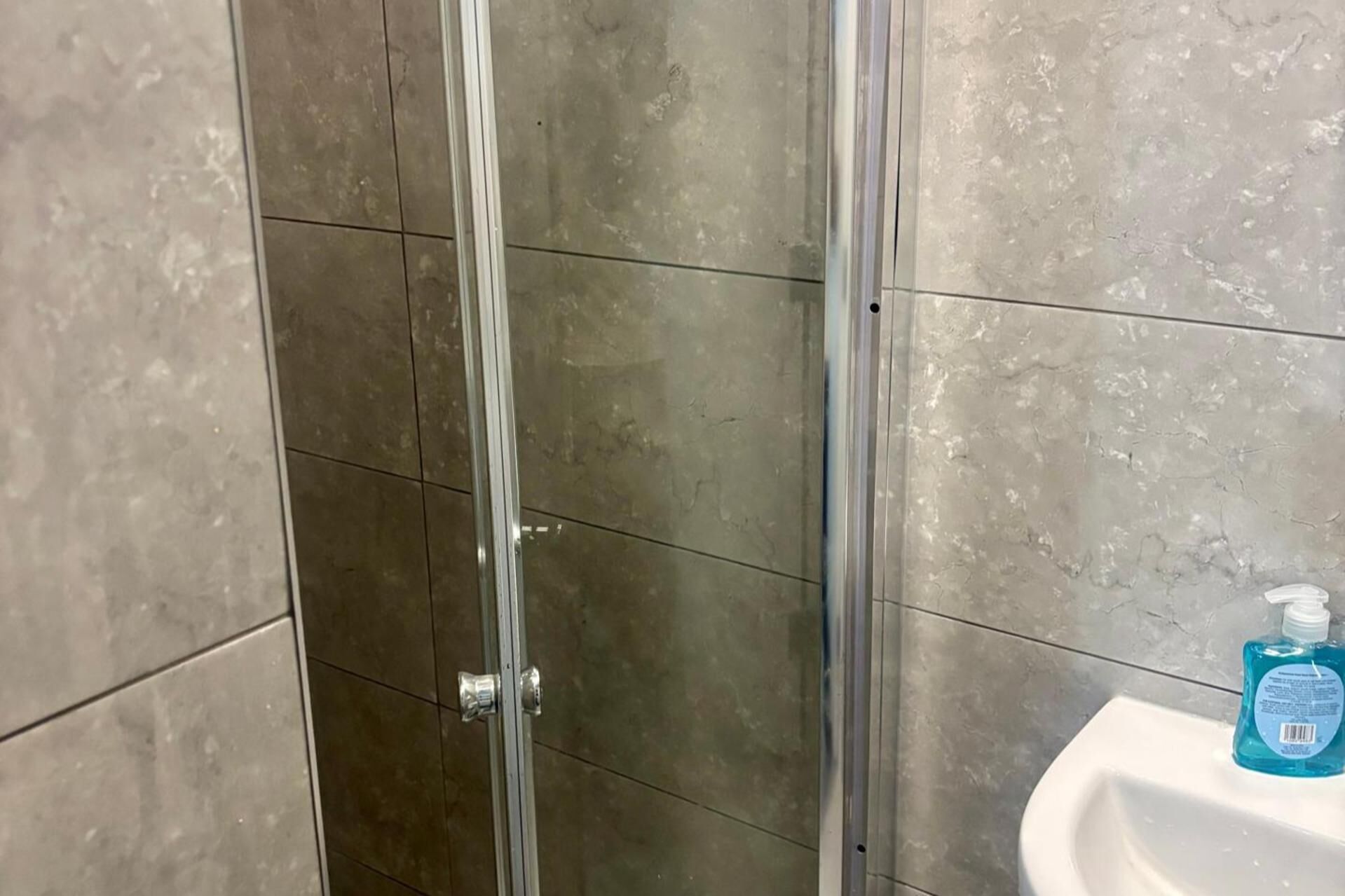 Ein Badezimmer mit Glasduschtür, Waschbecken und einer Handseifenflasche.