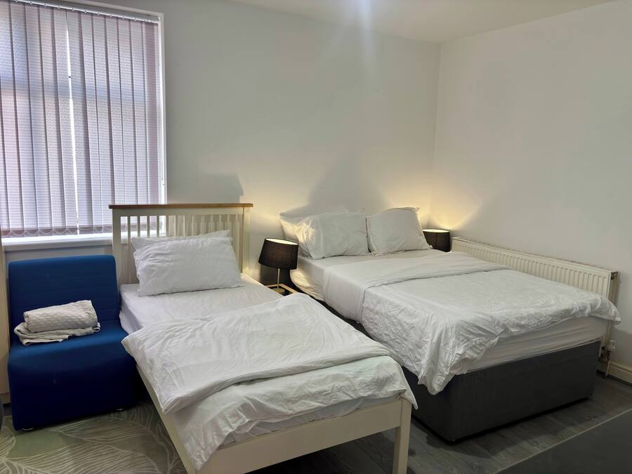 Un dormitorio con dos camas individuales, una silla azul, una lámpara de noche y una ventana con persianas.