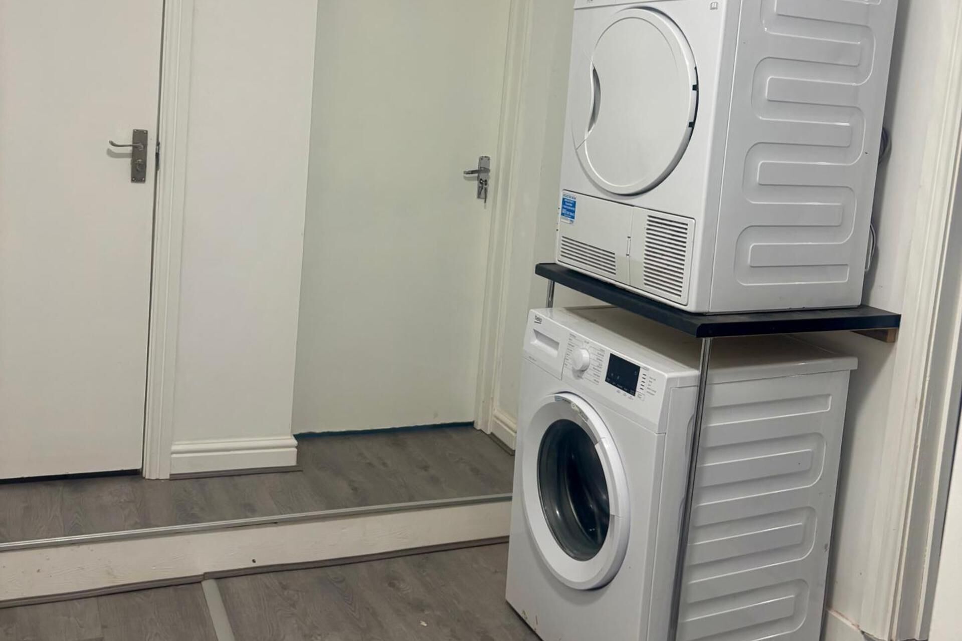 A laundry room with a front-loading washer and dryer stacked on a shelf.