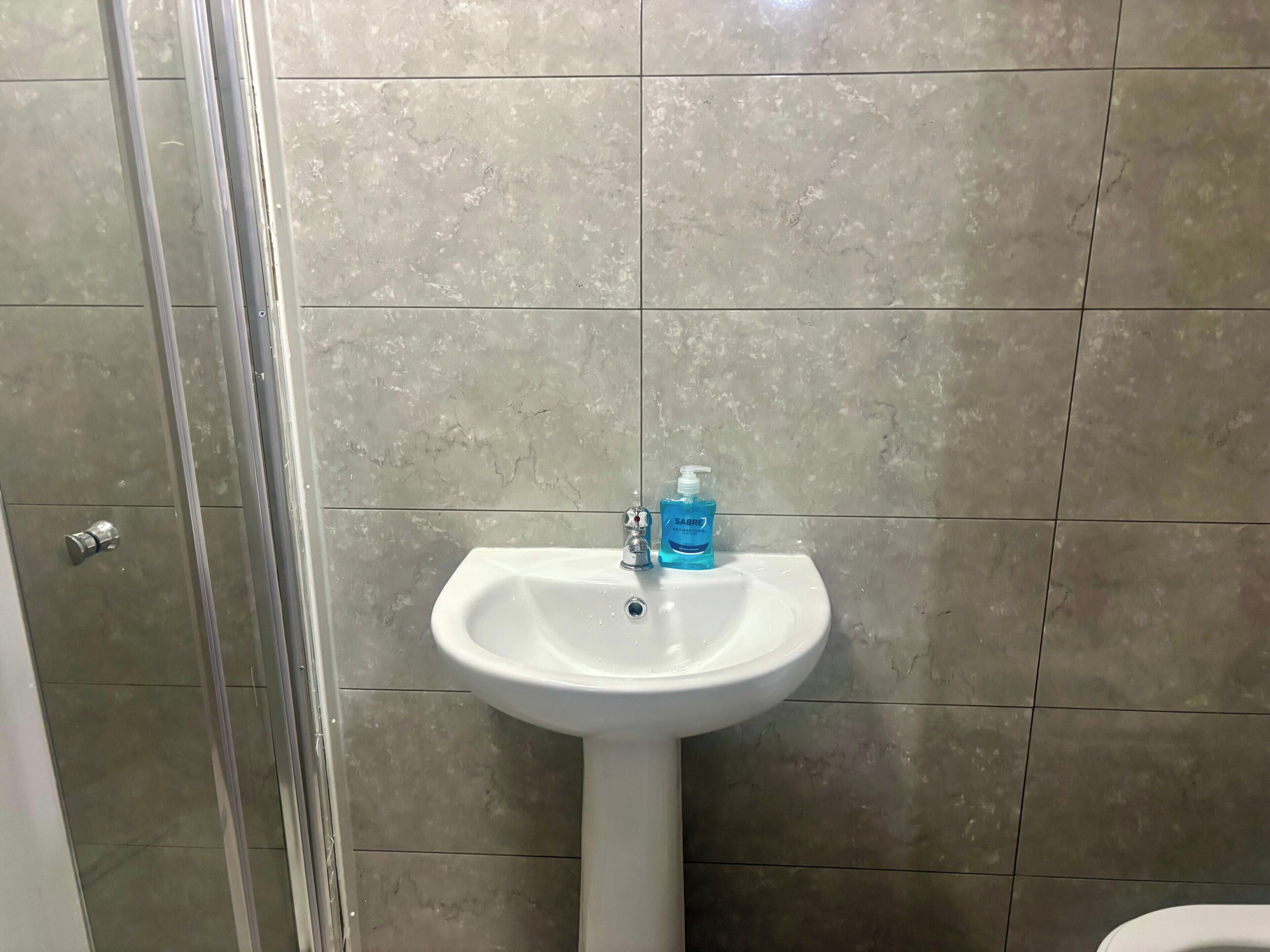 A bathroom with a white pedestal sink, a glass shower enclosure, and a tiled wall.