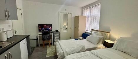 A hotel room with two beds, a desk with a television, a wardrobe, and a window with blinds.