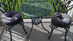 Una mesa redonda de metal con una superficie decorada, flanqueada por dos sillas con asientos acolchados.