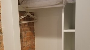 Un armario con pared de ladrillo, repisas blancas y espacio para colgar.