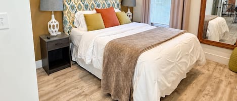 A bedroom with a bed, bedside tables, a patterned headboard, and a large mirror.
