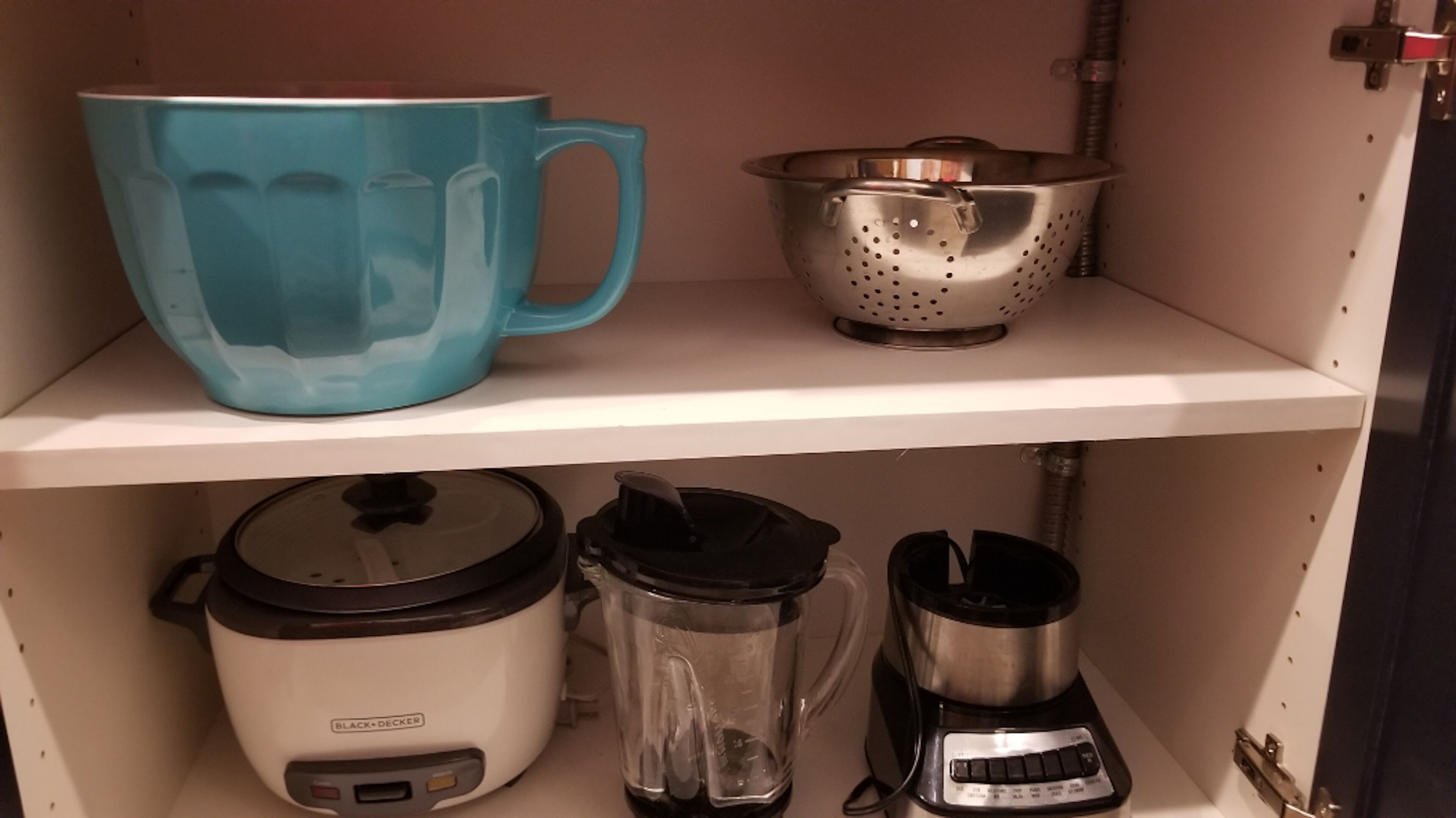 Une étagère de cuisine avec une tasse bleue, une passoire en acier inoxydable, une mijoteuse blanche, un mixeur et une machine à café.