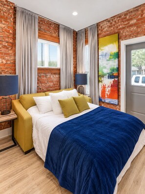 A hotel room with a brick wall, a bed with white and blue bedding, a yellow armchair, and a large abstract painting. - Comfy 1 Bedroom Apartment! Salt Lake City. Close to UofU (Salt Lake City)