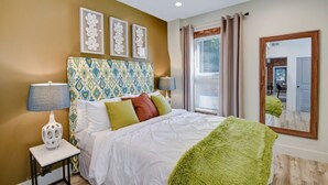 Habitación de hotel con cama, mesita de noche, lámpara, espejo y ventana con cortinas.